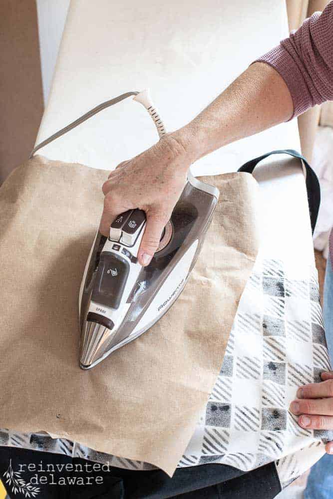 Lady ironing a stenciled tote bag with brown craft paper to protect the painted surface.