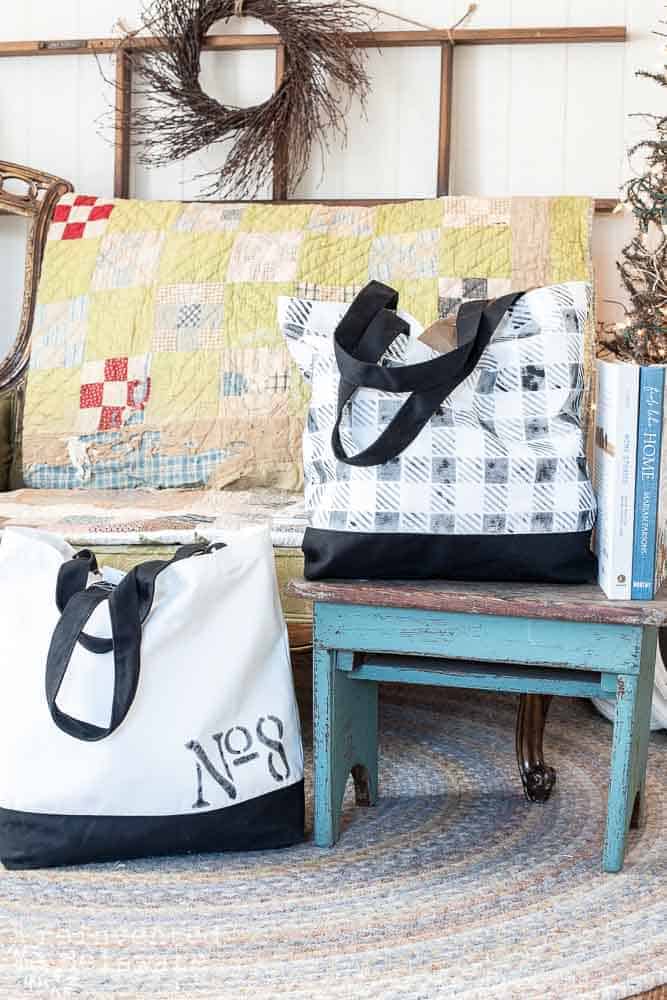 Two tote bags that have been stenciled and are staged with a step stool and a settee in the background.