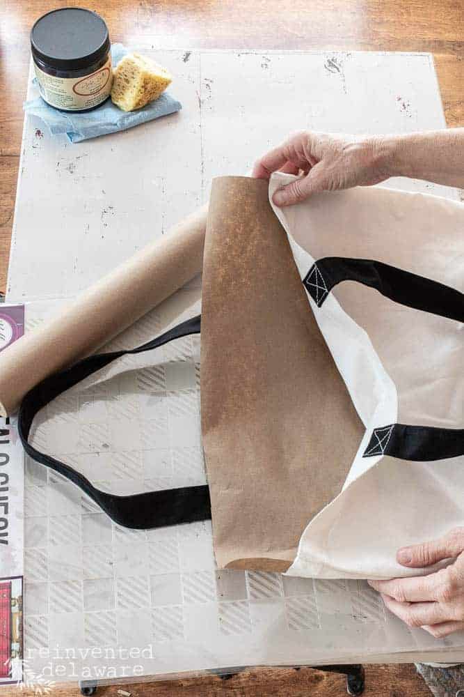 Lady putting a piece of craft paper inside a canvas tote bag for a fabric stencil project.