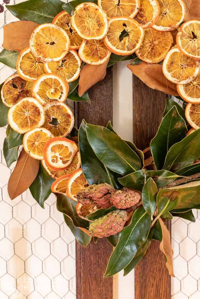 Close up view of easy diy magnolia leaf wreath with orange slices hanging on the wall with a frame.