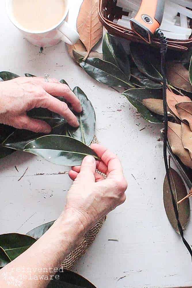 Lady showing how to glue magnolia leaves to the wreath frame.