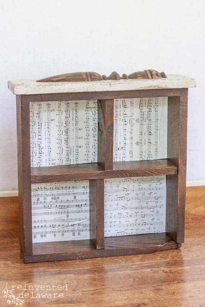 Vintage drawer upcycled into an organizer shelf with book page backing and table leg spindle added as decoration.