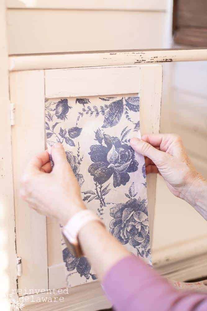 Lady dry fitting a piece of decoupage paper for furniture on a washstand.