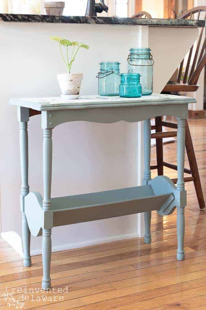 The after of an end table makeover idea showing the end table with vintage blue mason jars and a plant sitting on top.