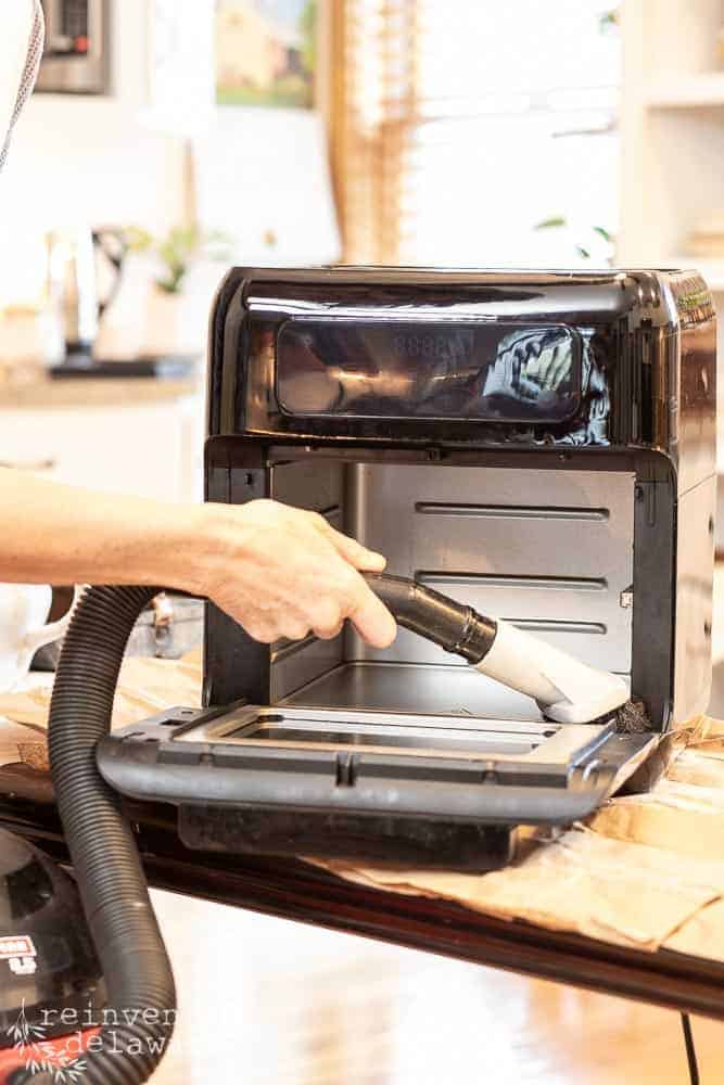 Lady vacuuming the inside of an air fryer with a shop vac.