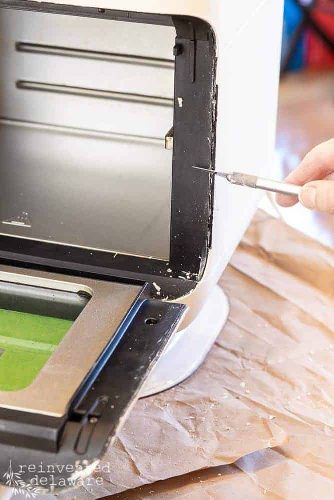 Lady scrapping off paint on the inside of a painted air fryer.