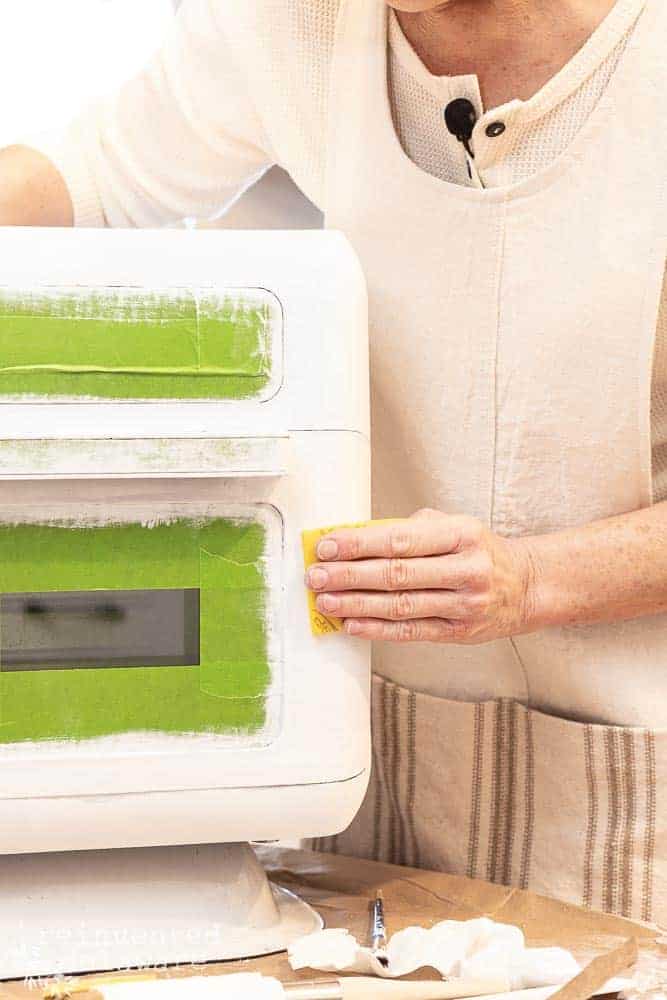 Lady sanding between coats of paint on an air fryer for a DIY kitchen appliance makeover tutorial.