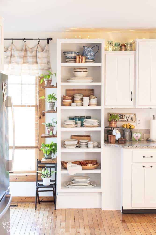 Open shelving that has been painted for a cabinet painting blog post tutorial. Shelves filled with ironstone dishes, cutting boards and fresh pothos plants.