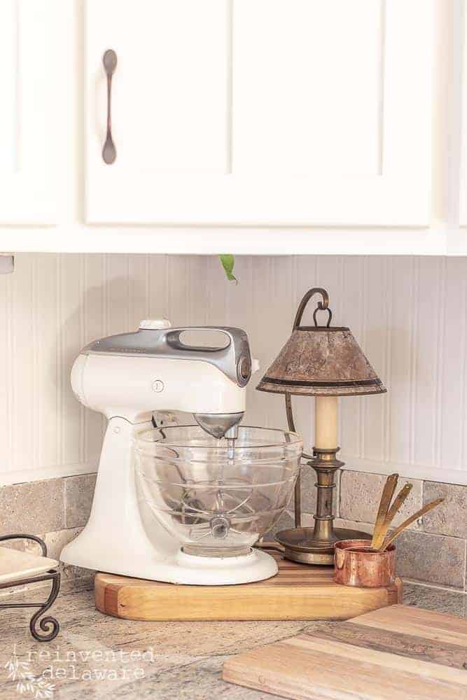 Close up of antique Kitchen Aid stand mixer, vintage brass lamp, copper measuring cups and handmade cutting board.