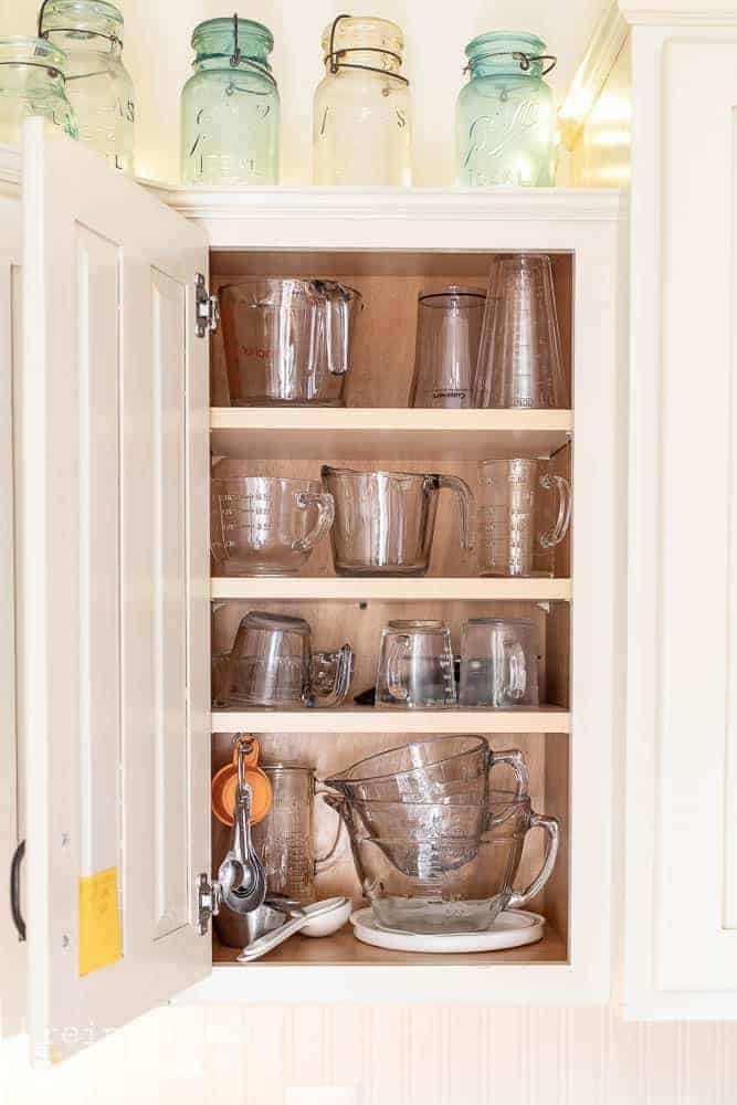 Interior of kitchen cabinet with organized vintage glass measuring cups.