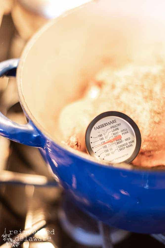 Close up of a food thermometer stuck in a roasted chicken in a dutch oven.
