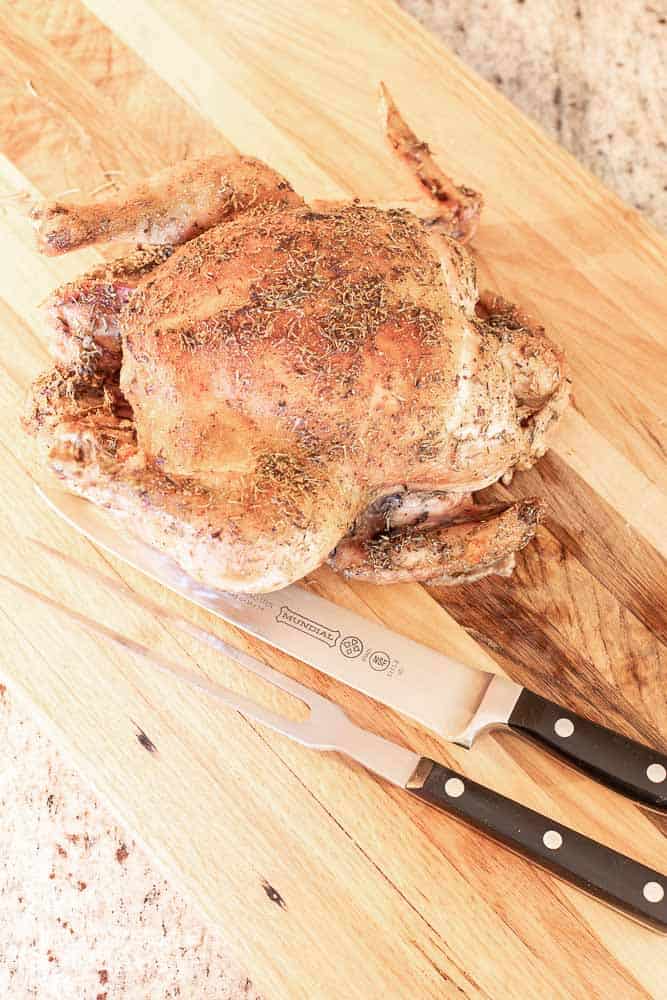A whole roasted chicken on a cutting board with a chef's knife and chef's fork.