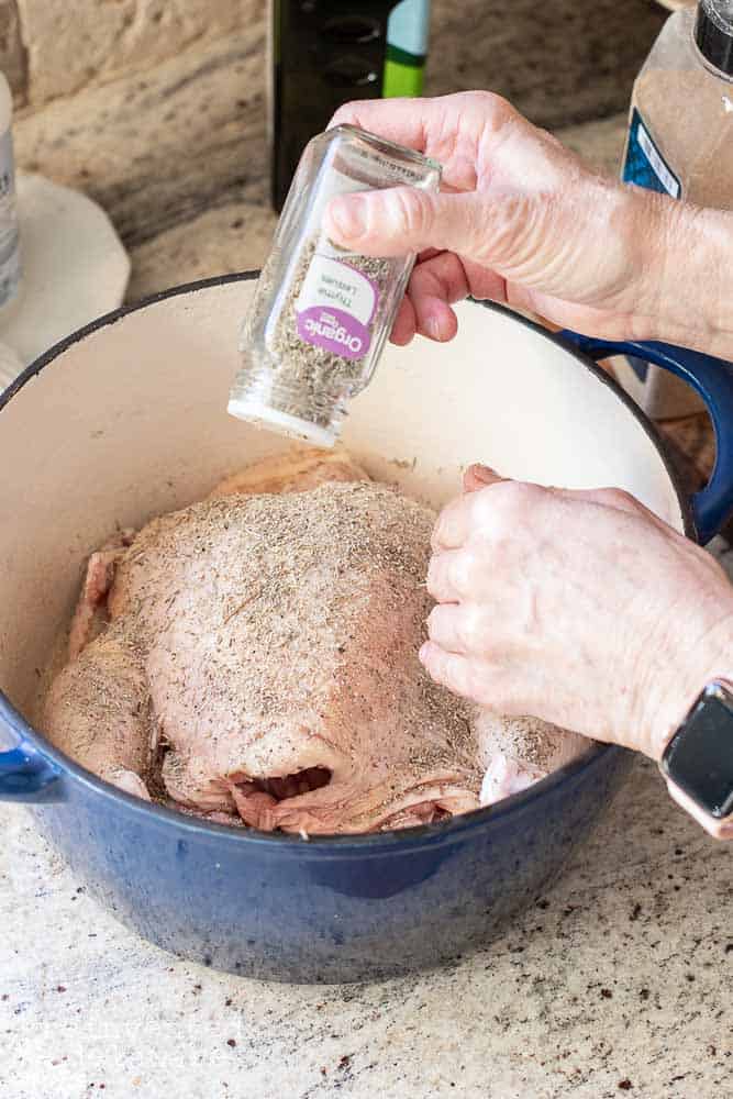 Lady sprinkling spices on the raw chicken in an enamel covered cast iron dutch oven.