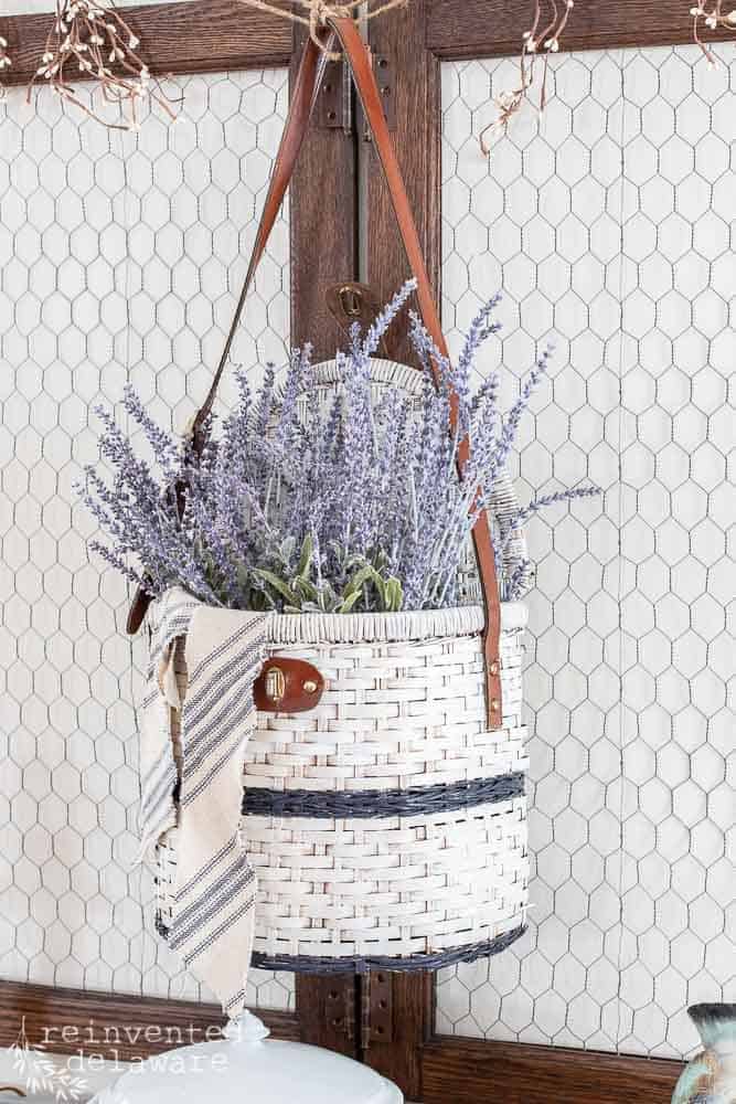 Picnic Basket upcycle with faux lavender inside and a grainsack ribbon hanging on the edge.