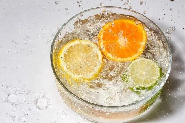 Clear bowl filled with sparkling water and a lemon slice, orange slice and a lime slice.