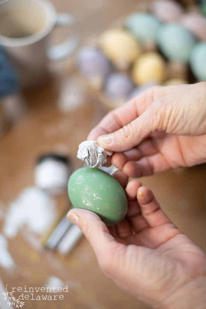 Lady using a piece of paper towel to dab on metaillic Dixie Belle Mouse on a painted wooden egg.