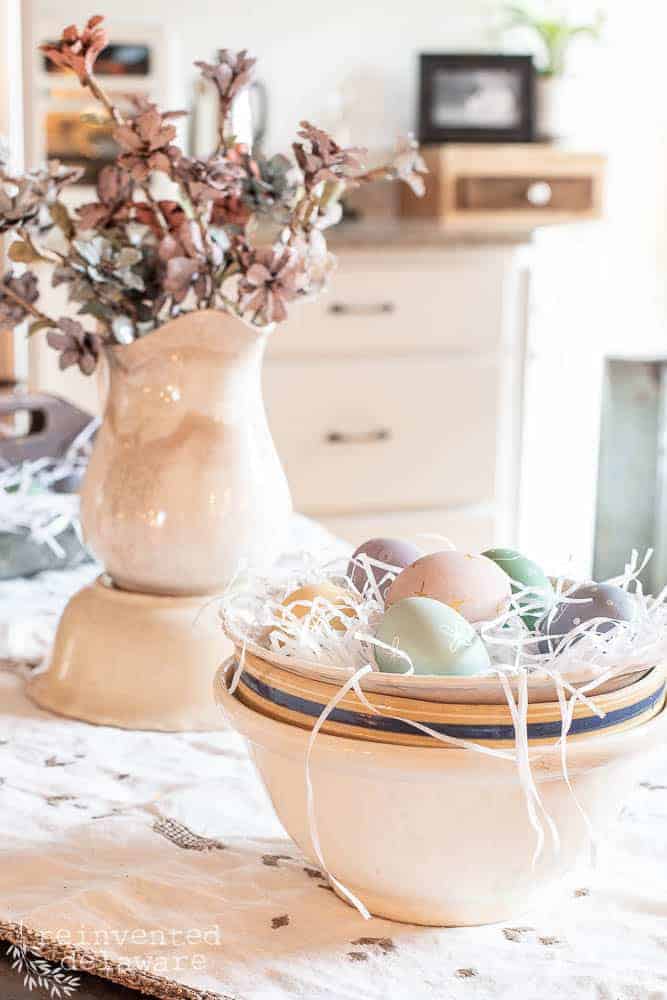 Hand painted wooden eggs in a round bowl with pine cone flowers in the background.