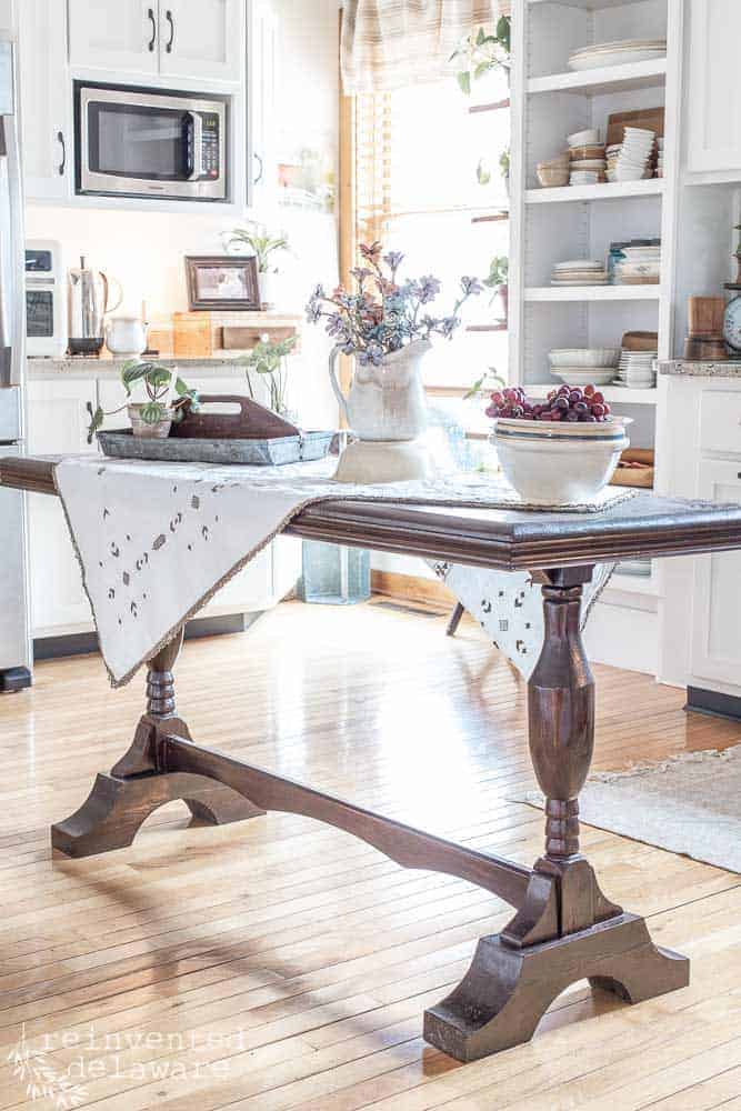 Table in a kitchen with pine cone table decorations sitting on top.