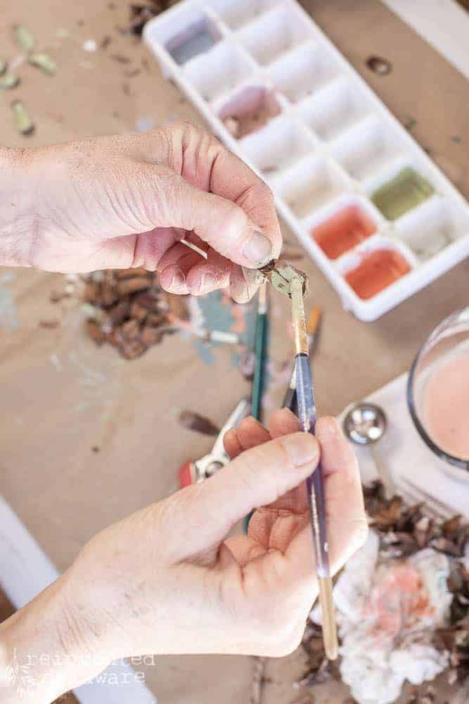 Lady painting sections of pine cone petals to be leaves in a pine cone flower arrangment.