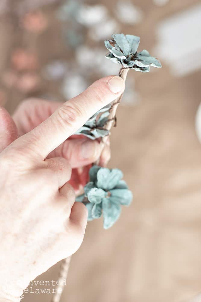 Lady showing where to glue the top flower on a pine cone table decorations flower arrangement.