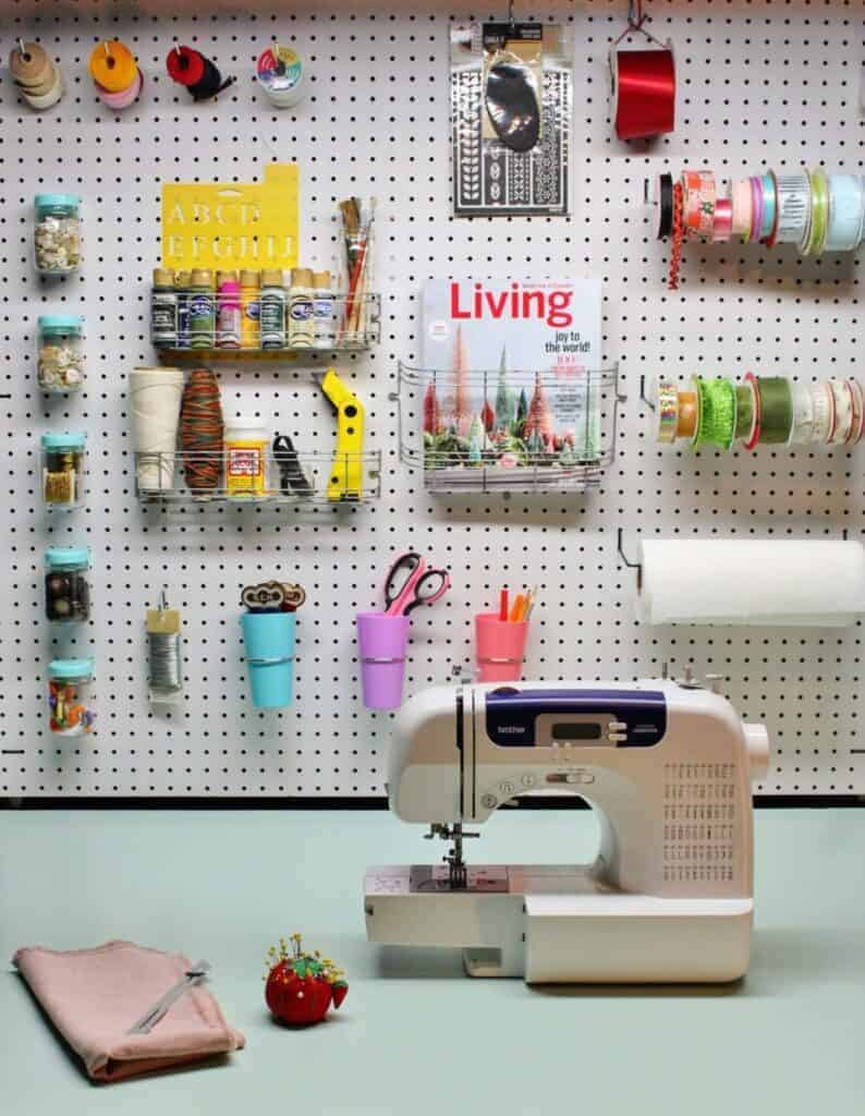 Sewing machine on a craft table with a pegboard wall filled with craft and sewing supplies.