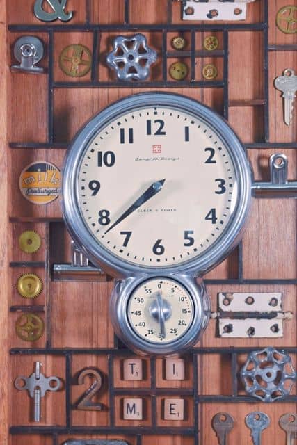 Antique clock with other upcycled vintage items in a printers draw hanging on a wall.