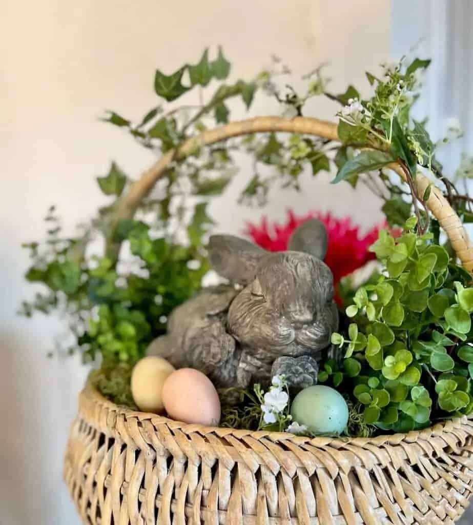 Basket filled with concrete bunny, painted eggs and greenery.