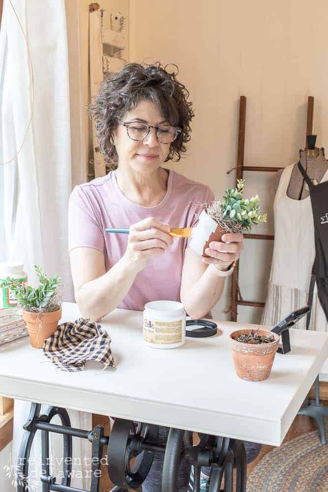 Lady painting a terra cotta pot to show off a repurposed sewing cabinet base turned into a craft table.