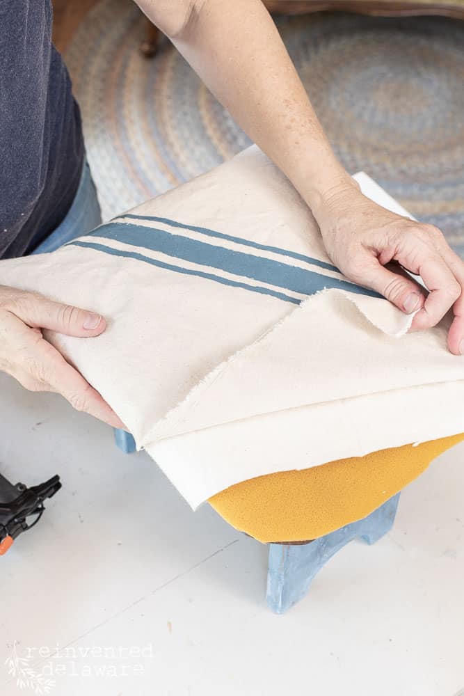 Lady adding upholstery layers to a wood footstool for a DIY footstool idea blog post.