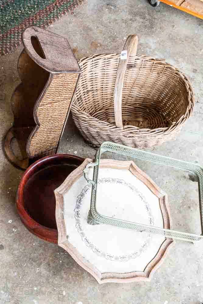 pile of thrift store home decor pieces including wooden basket, vintage silver plated serving dish, broken table