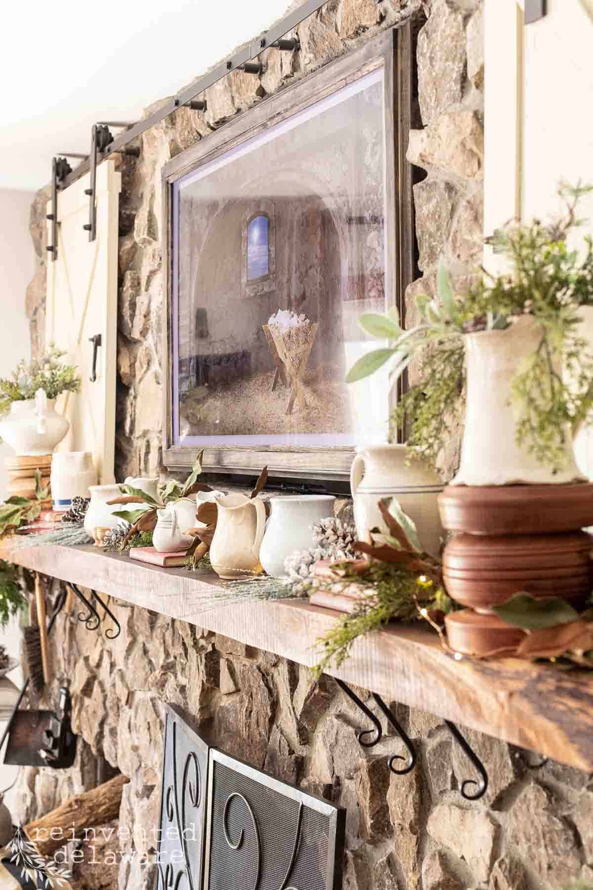 fireplace mantle decorated with vintage ironstone pitchers, fresh greenery, faux greenery and handmade candle holders with a Frame Tv above the fireplace mantle showing simple vintage inspired Christmas home tour ideas