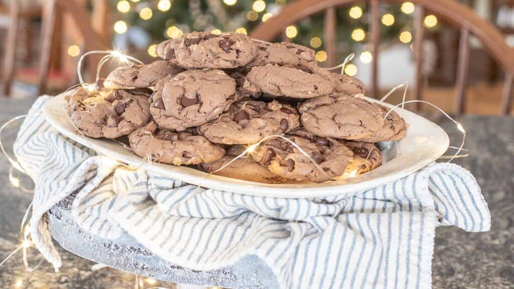 A white plate piled with chocolate chip cookies made from cake mix rests on a blue and white striped cloth. Delicate string lights adorn the plate, casting a glowing, festive background.