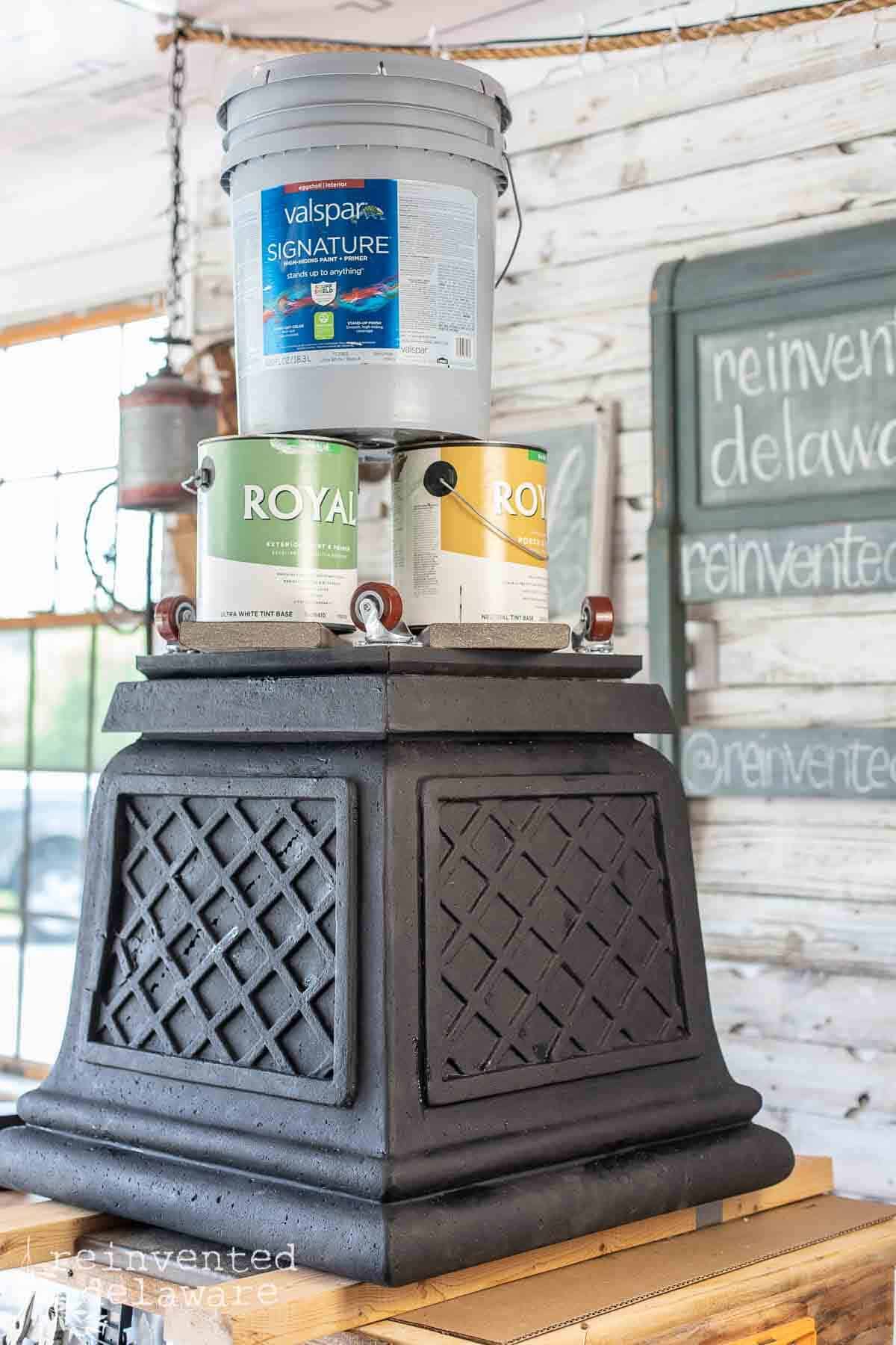 paint cans stacked on top of upcycled outdoor patio planter while glue dries