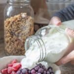 homemade greek yogurt in a glass jar with frozen berries in a small bowl