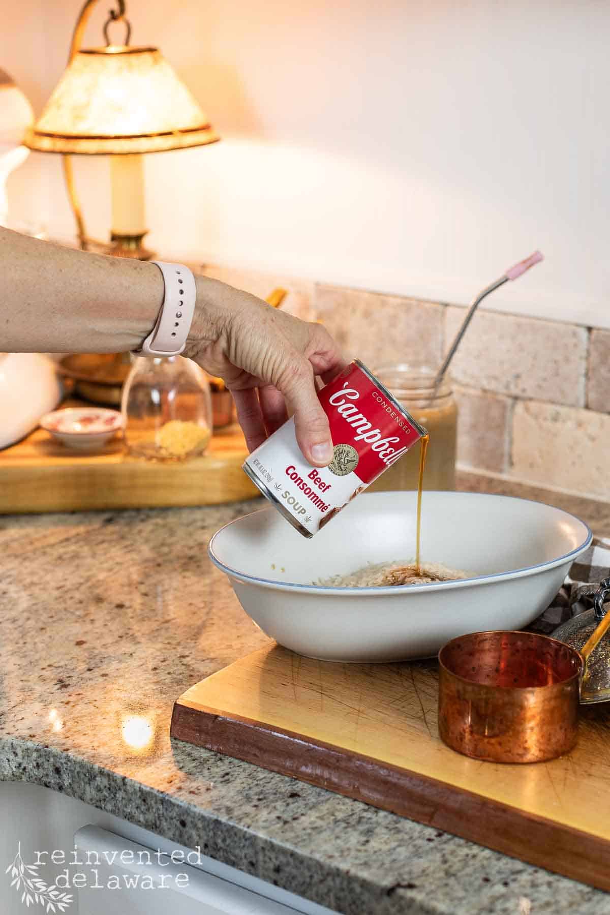 lady pouring beef consomme soup into dish with rice