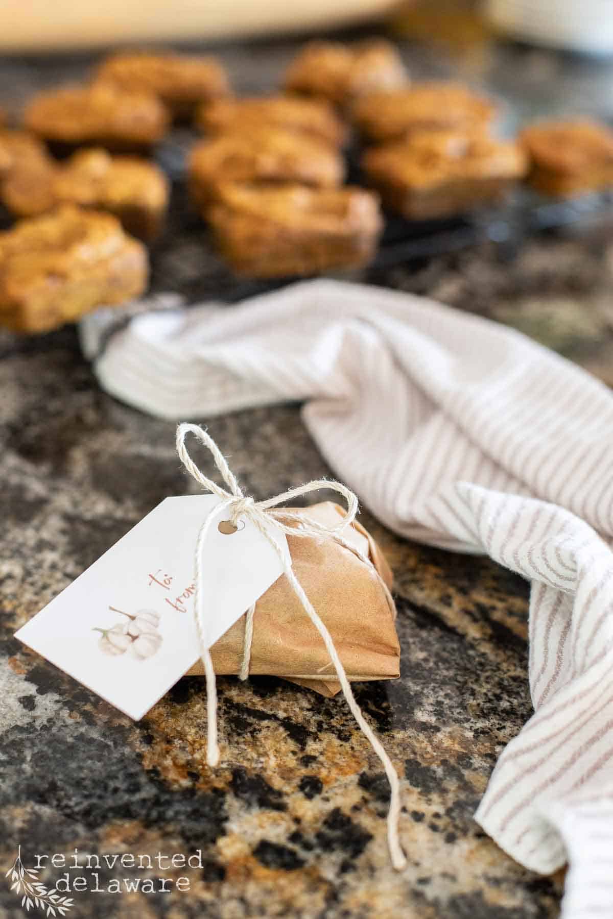 A mini pumpkin bread loaf wrapped in parchement paper with a free printable gift tag tied on to secure the package.