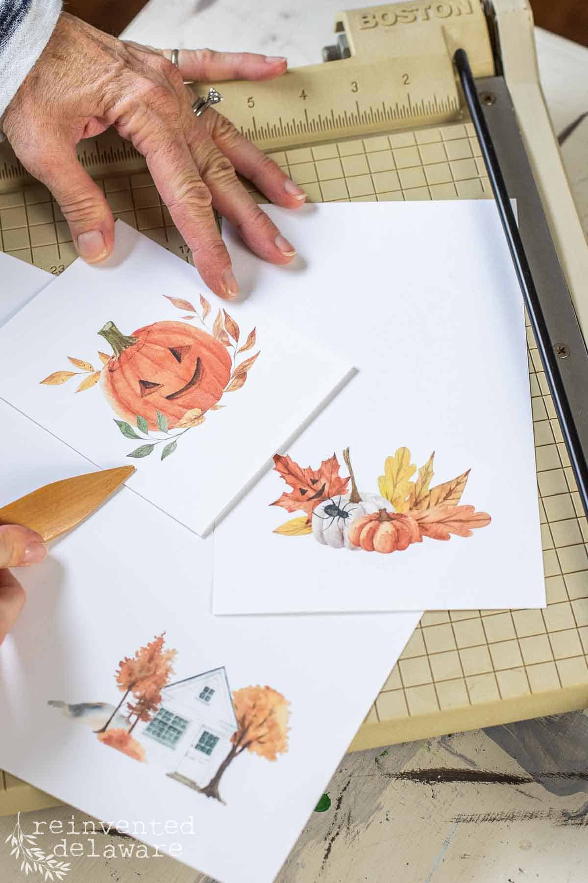 A lady making free printable greeting cards for fall and using a folding tool to crease the paper.