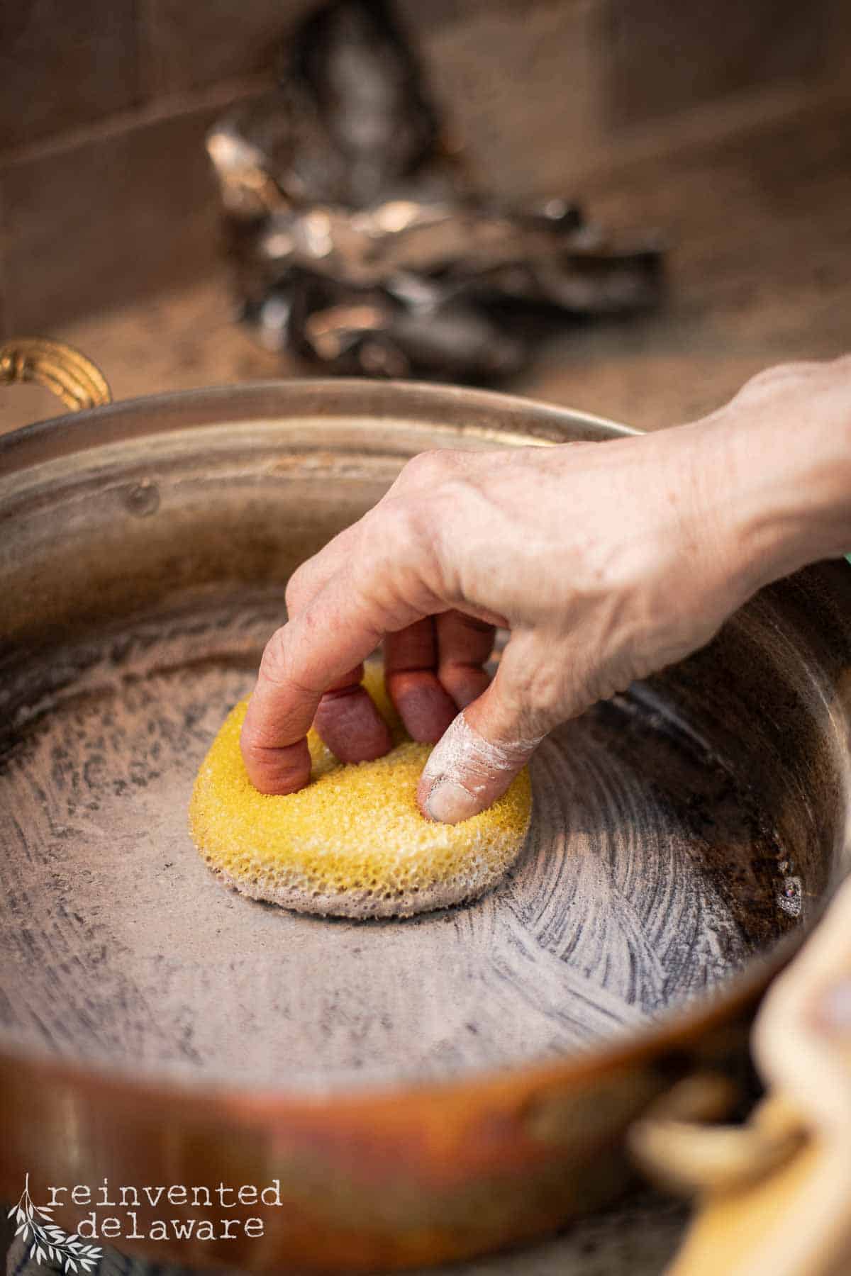 lady using a soft abrasive cleaner to clean a tin lined copper pot
