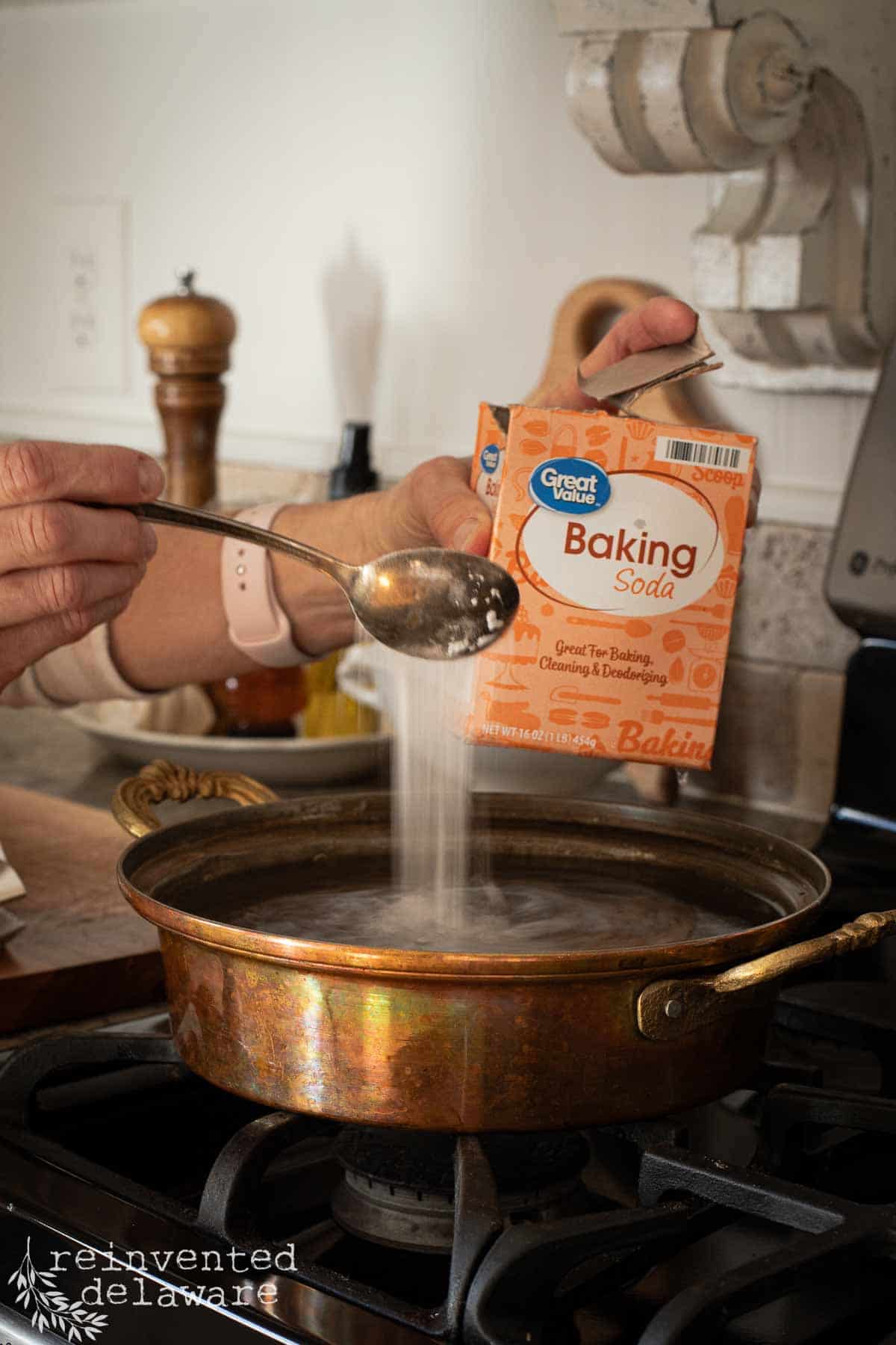 lady adding baking soda to water in a burnt copper pan to clean it