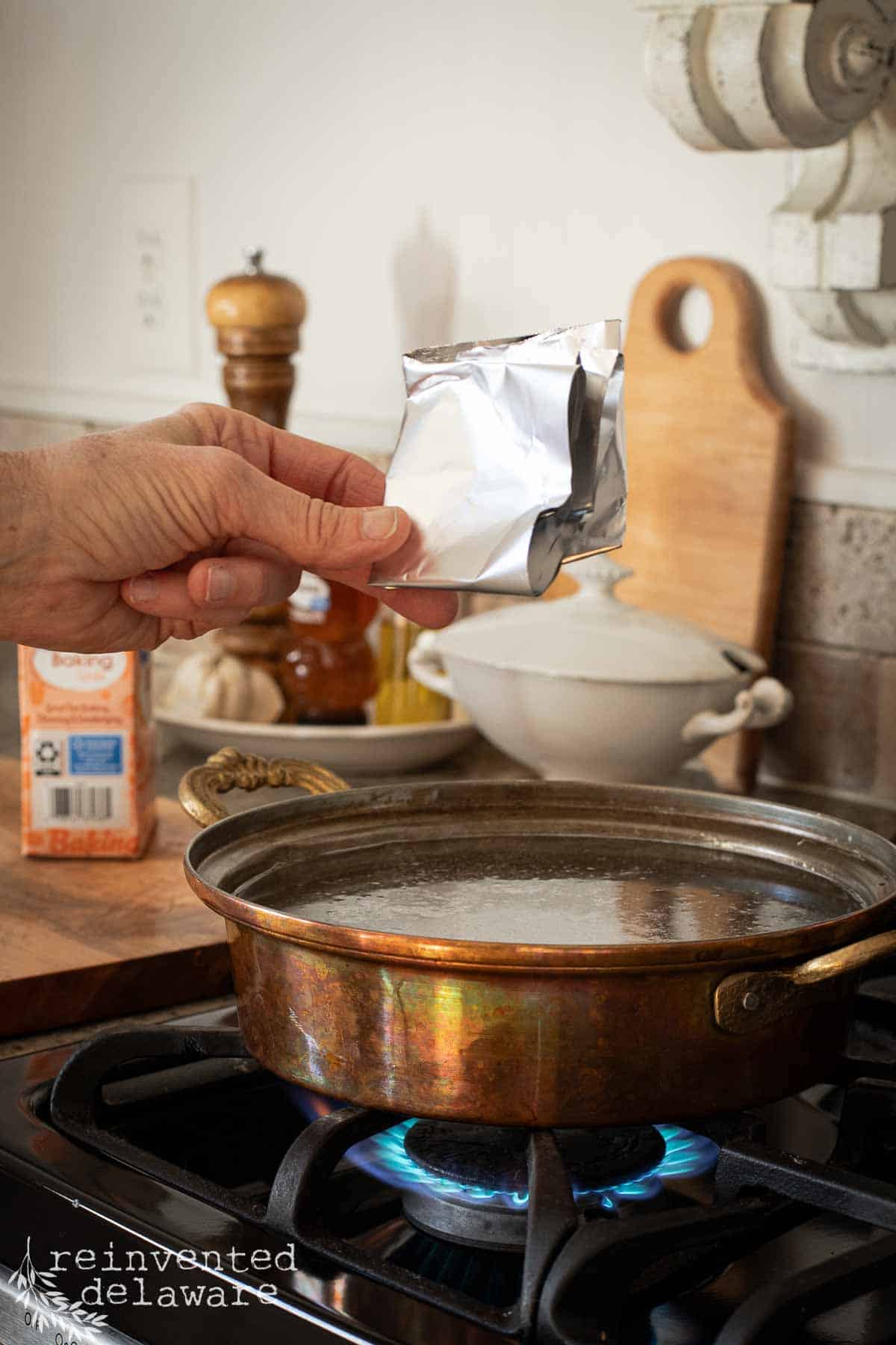 lady adding a folding piece of aluminum foil to water in a copper pan to clean the tin lining