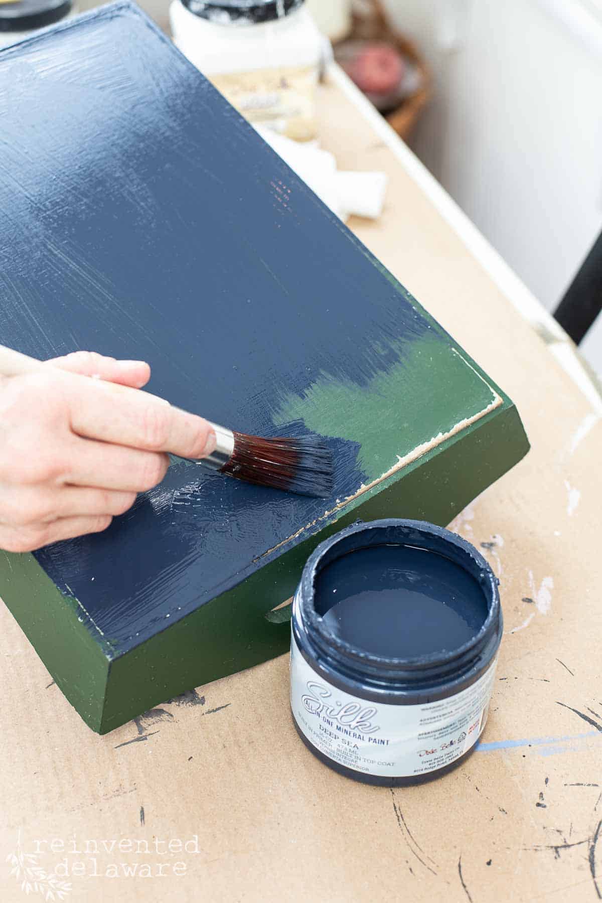 lady painting a thrift store tray in navy chalk paint for an upcycled home decor project