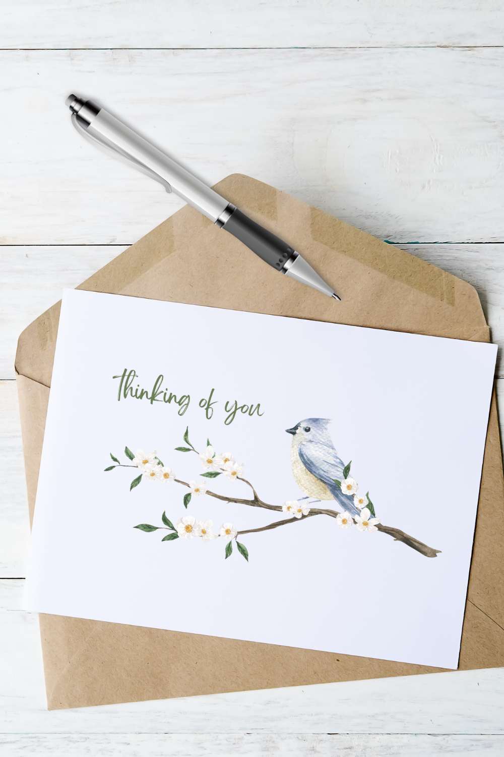 greeting card with a bird sitting on a branch design laying on top of brown envelope and ink pen