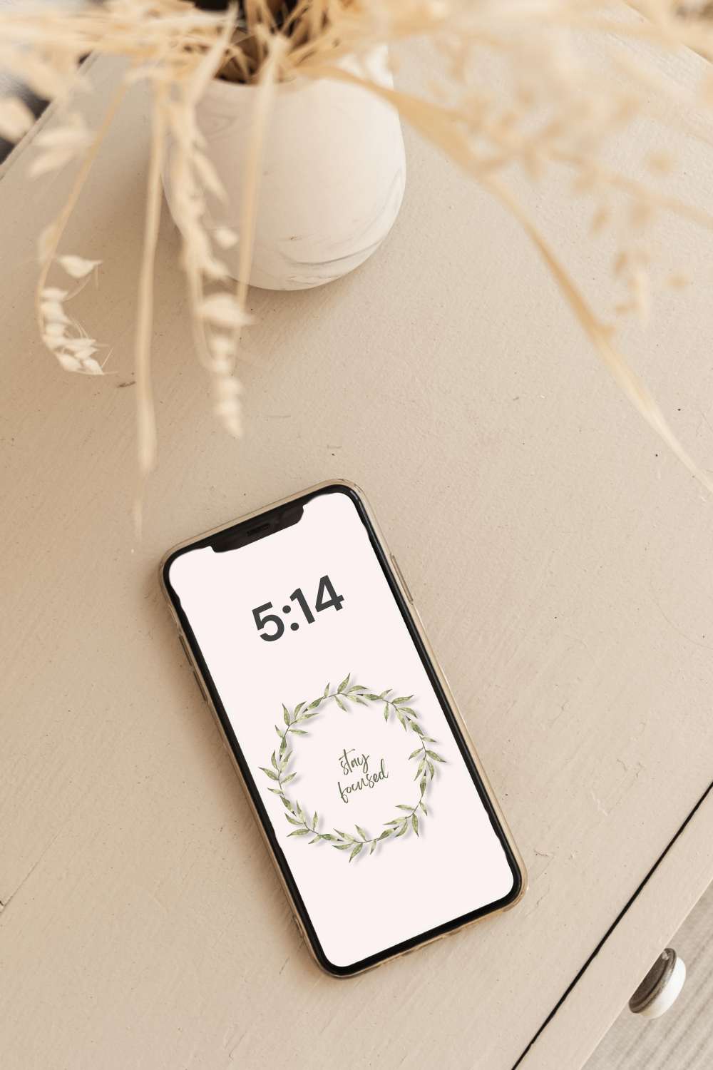 iphone with digital art on the screen sitting on a desk with vase of flowers