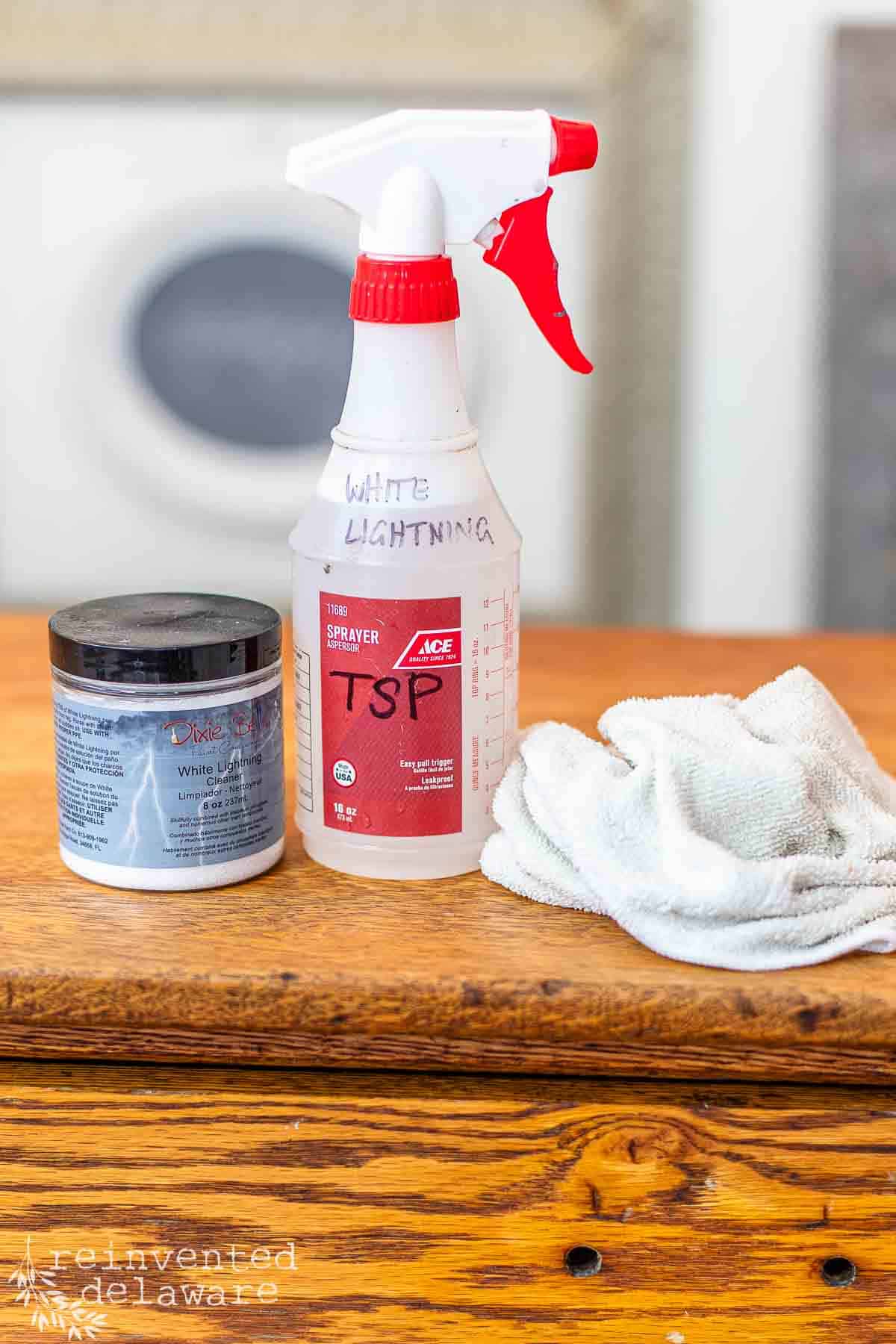 spray bottle filled with TSP cleaning solution, jar of dry TSP powder and a microfiber cloth used to clean furniture for makeovers