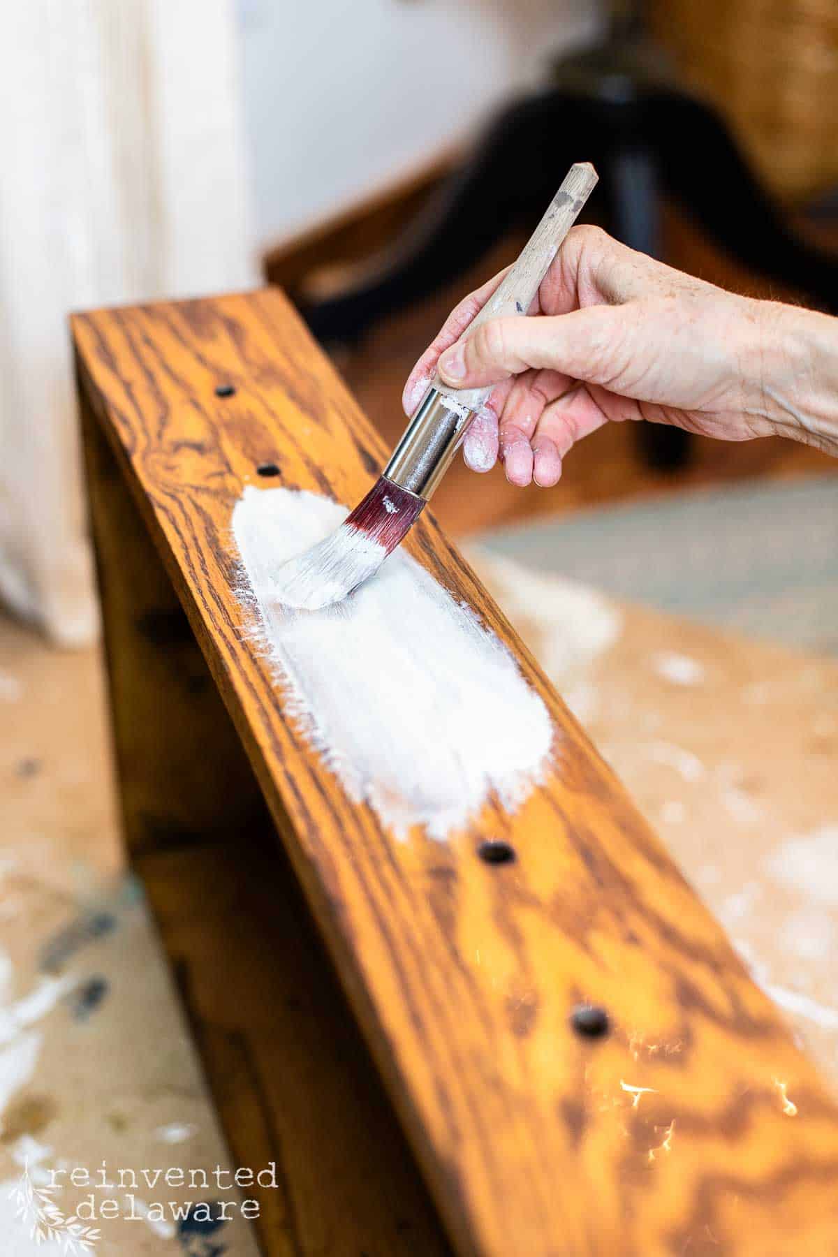 lady applying chalk paint to a wood furniture piece for a makeover project showing how to whitewash oak furniture.