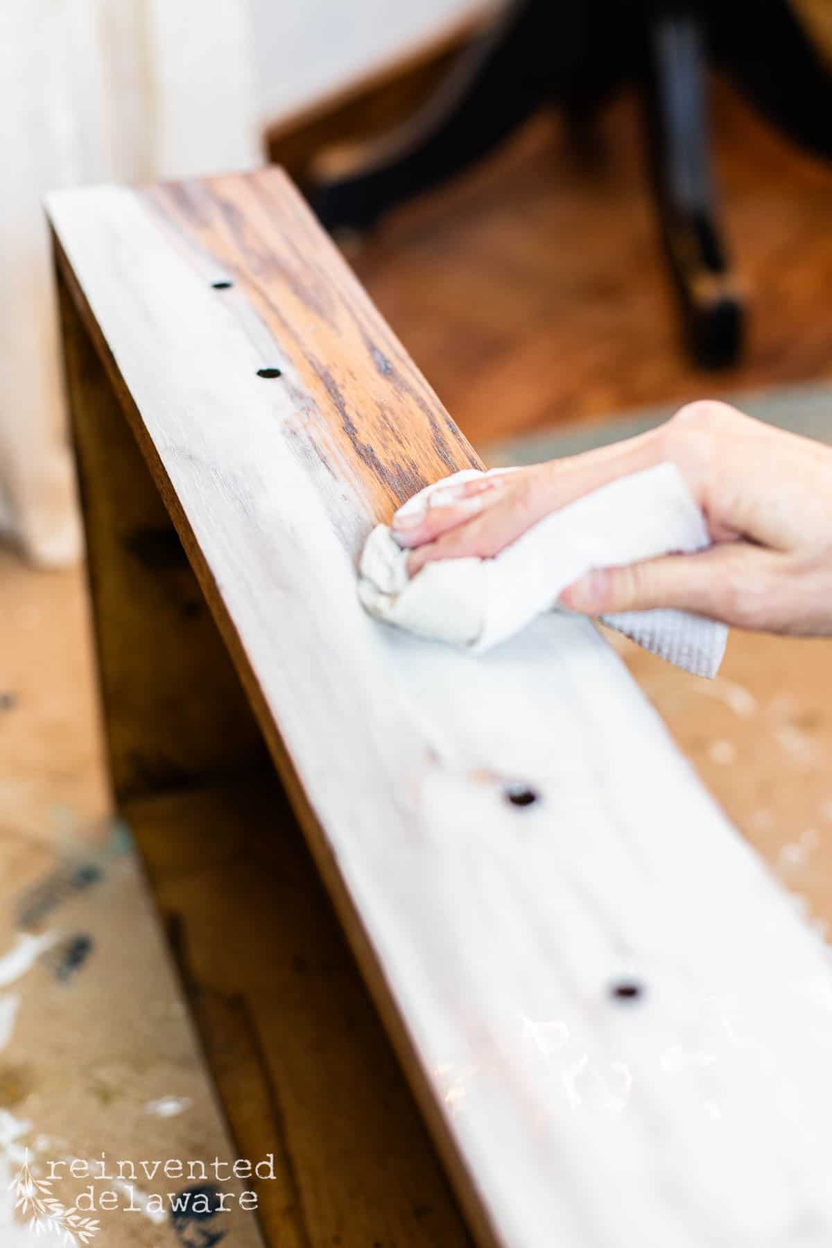 lady wiping back excess chalk paint during a whitewashing paint technique on an old piece of furniture