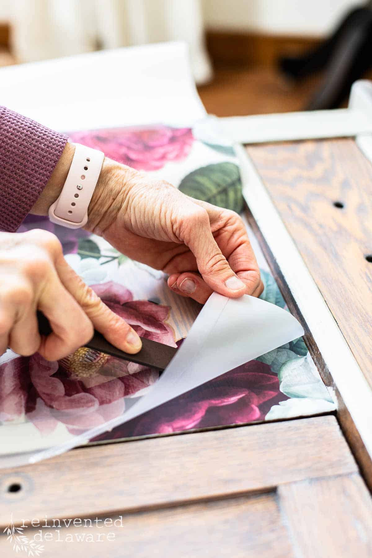 lady applying a furniture transfer to an old washstand for a floral decorative accent.