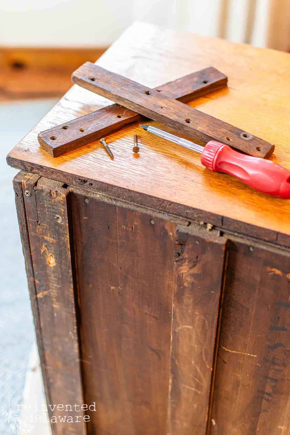 spare wood parts of old washstand used to hold a harp on the back sitting on top of washstand with a screwdriver and old screws.