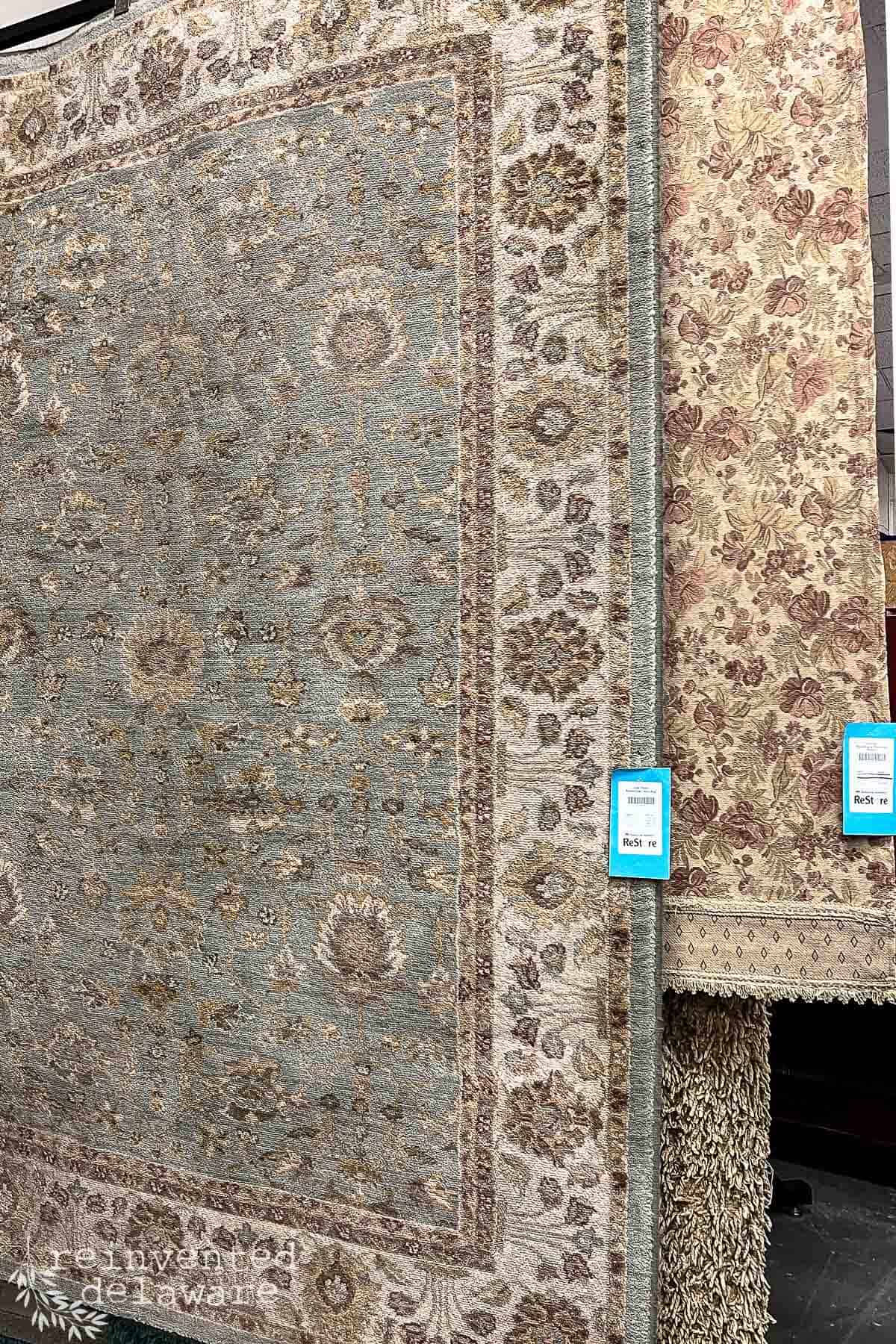 large used rug in vintage colors hanging on a rack in a Restore