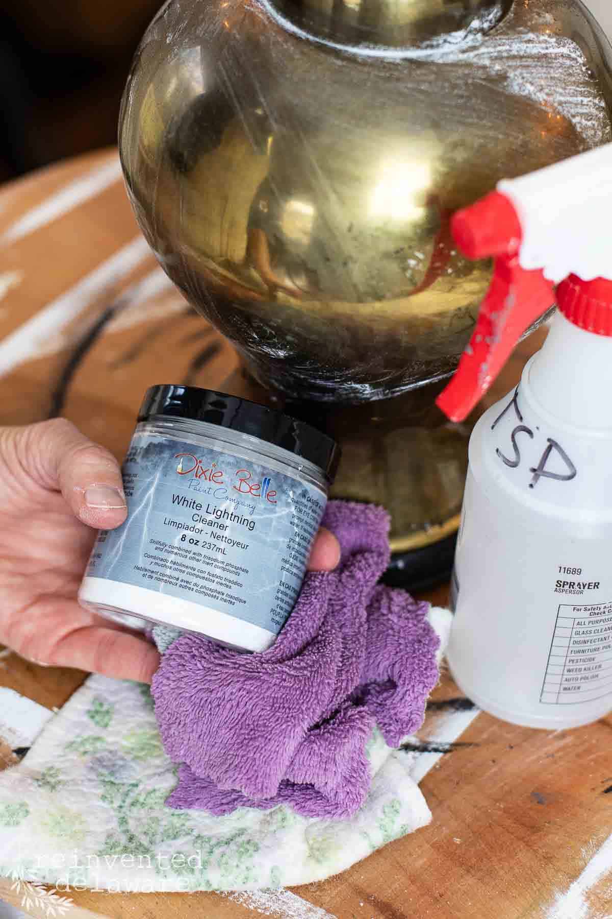 Lady showing a jar of White Lightning TSP cleaner with a spray bottle and an old dirty lamp in the background.